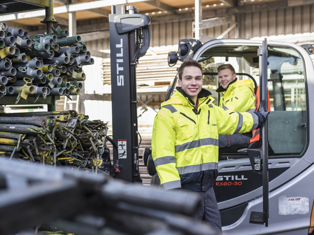 Zwei Mitarbeiter vor den Produktionshallen von Lindner kümmern sich mithilfe eines Gabelstaplers um die Materialorganisation